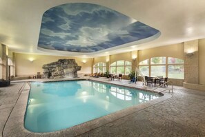 An indoor swimming pool with a stone wall and a rock formation, surrounded by lounge chairs and tables. - Luxe Chalet - Sleeps 15 (Midway)
