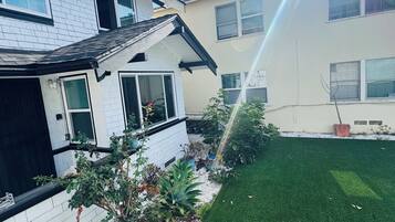Una casa de dos pisos con fachada blanca, césped verde y diversas plantas en macetas.