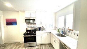 Una cocina moderna con armarios blancos, estufa de acero inoxidable y un ventanal grande.