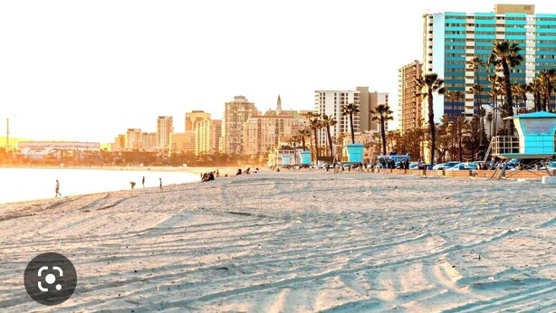 Una playa con un horizonte urbano al fondo, que incluye edificios altos y palmeras.
