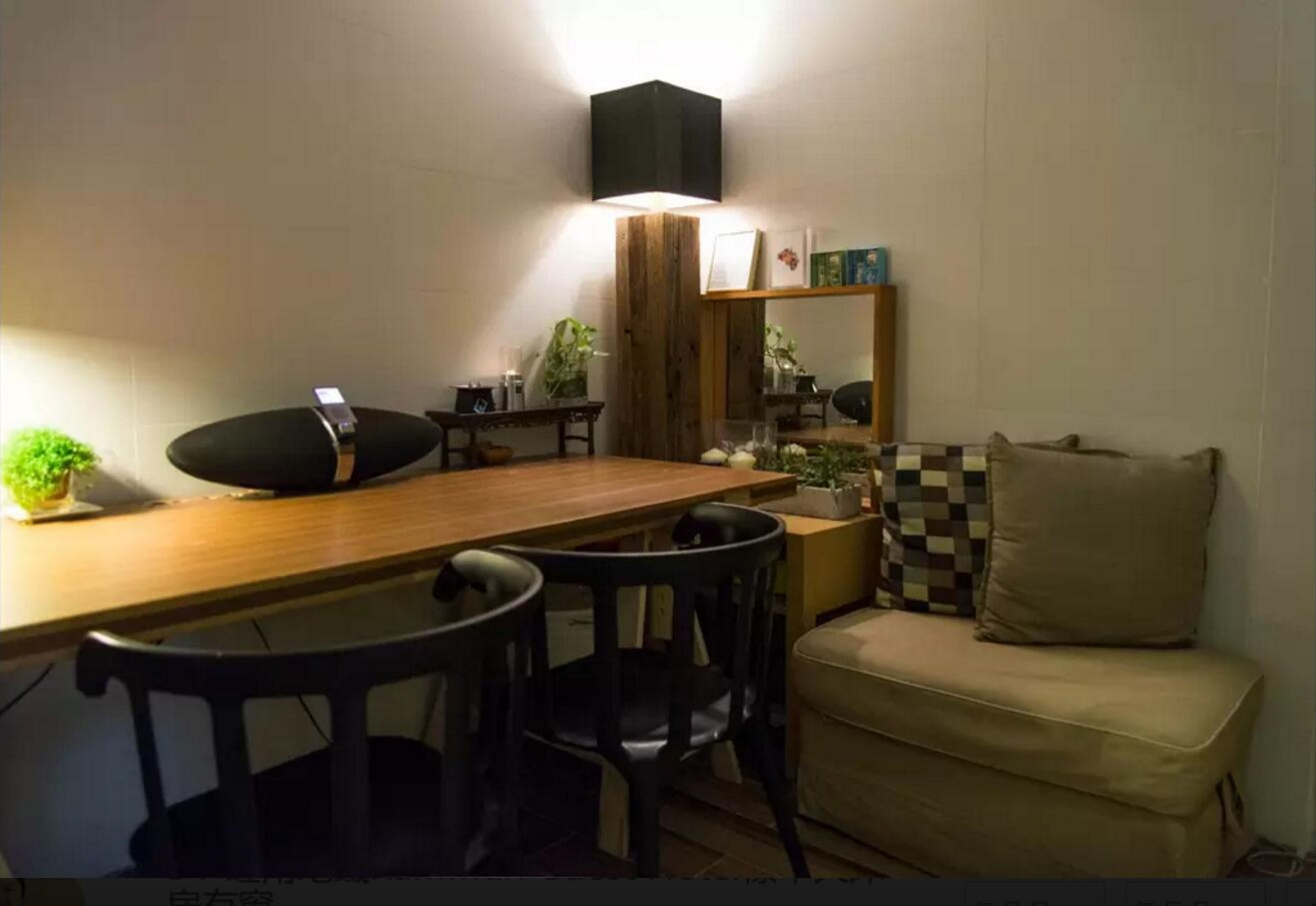 Un comedor acogedor con una mesa de madera, sillas negras, un pequeño sofá y un estante en la pared con libros y objetos decorativos.