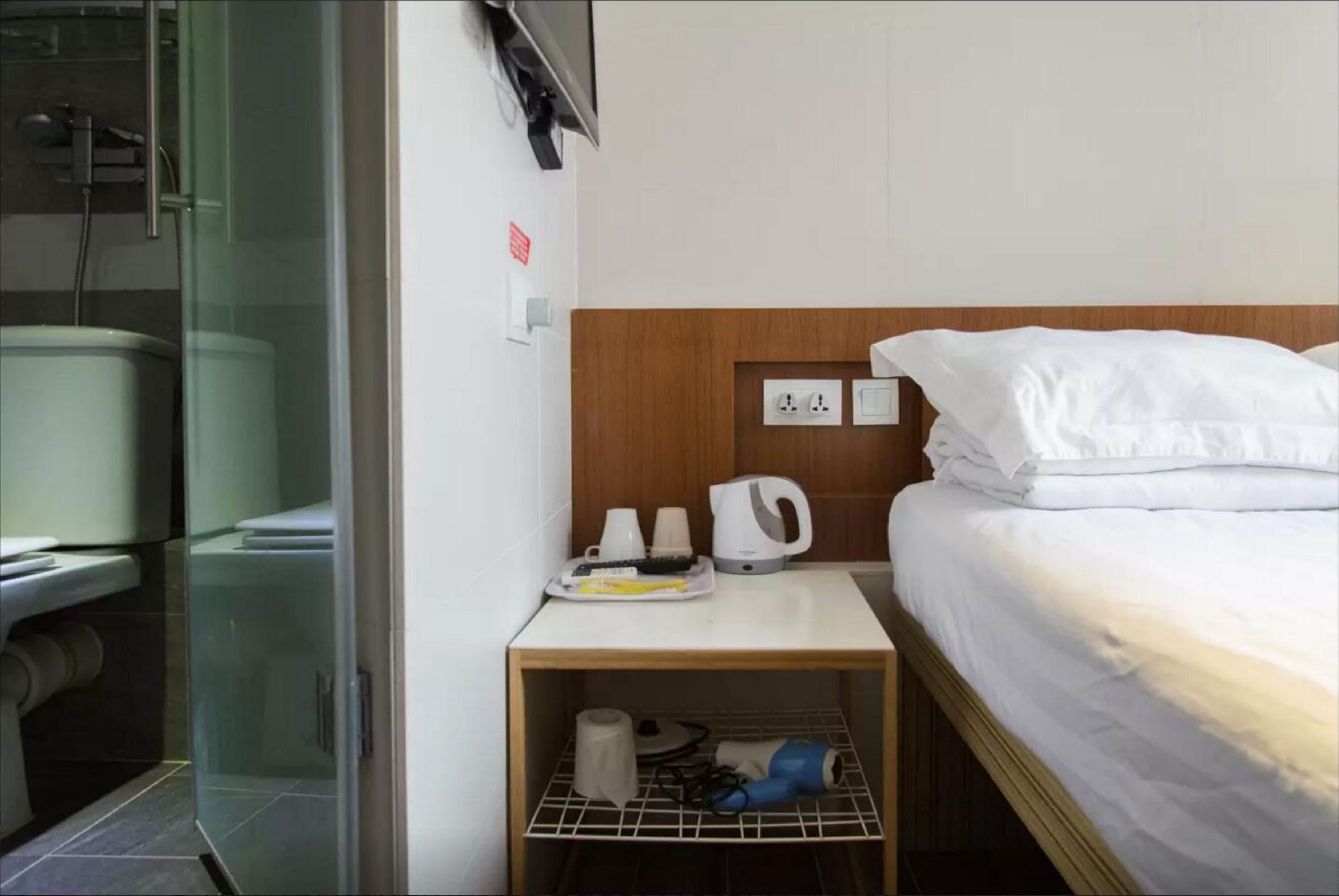 A hotel room with a bed, a small table with a kettle, cups, and a hairdryer.