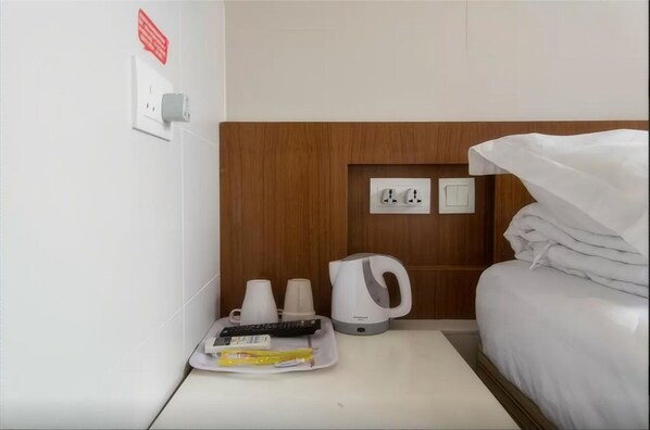 A hotel room with a bed, a tray with remote controls, cups, a kettle, and a power outlet. - Kam Mun Guest House (Kowloon)