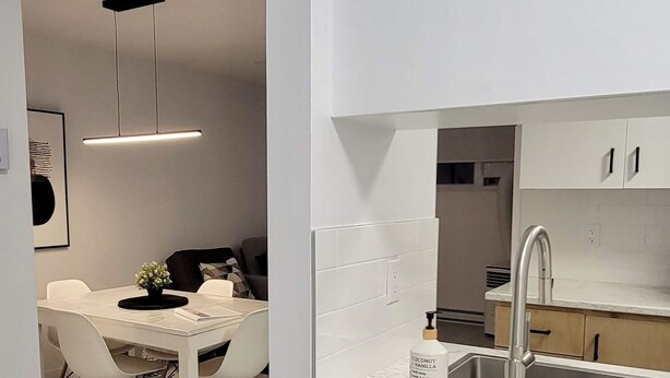 A modern kitchen with white cabinetry, a stainless steel sink, and a wooden dining table with chairs. - MONTSKI | Luxurious 〽️ condo (Beaupré)