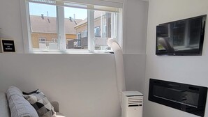 A modern living room with a sofa set, a TV mounted on the wall, and a window with a view of buildings outside. - MONTSKI | Luxurious 〽️ condo (Beaupré)
