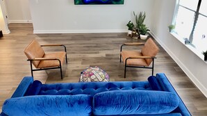 A modern living room with a blue sofa, two leather chairs, a colorful rug, and a wall-mounted TV displaying 'MASTERS'. - Modern Ranch-Style Retreat — Prime location for the Course ⛳️ (Augusta)