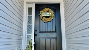 A dark front door with a wreath and a sign that reads "ANYTIME IS TEA TIME". - Modern Ranch-Style Retreat — Prime location for the Course ⛳️ (Augusta)