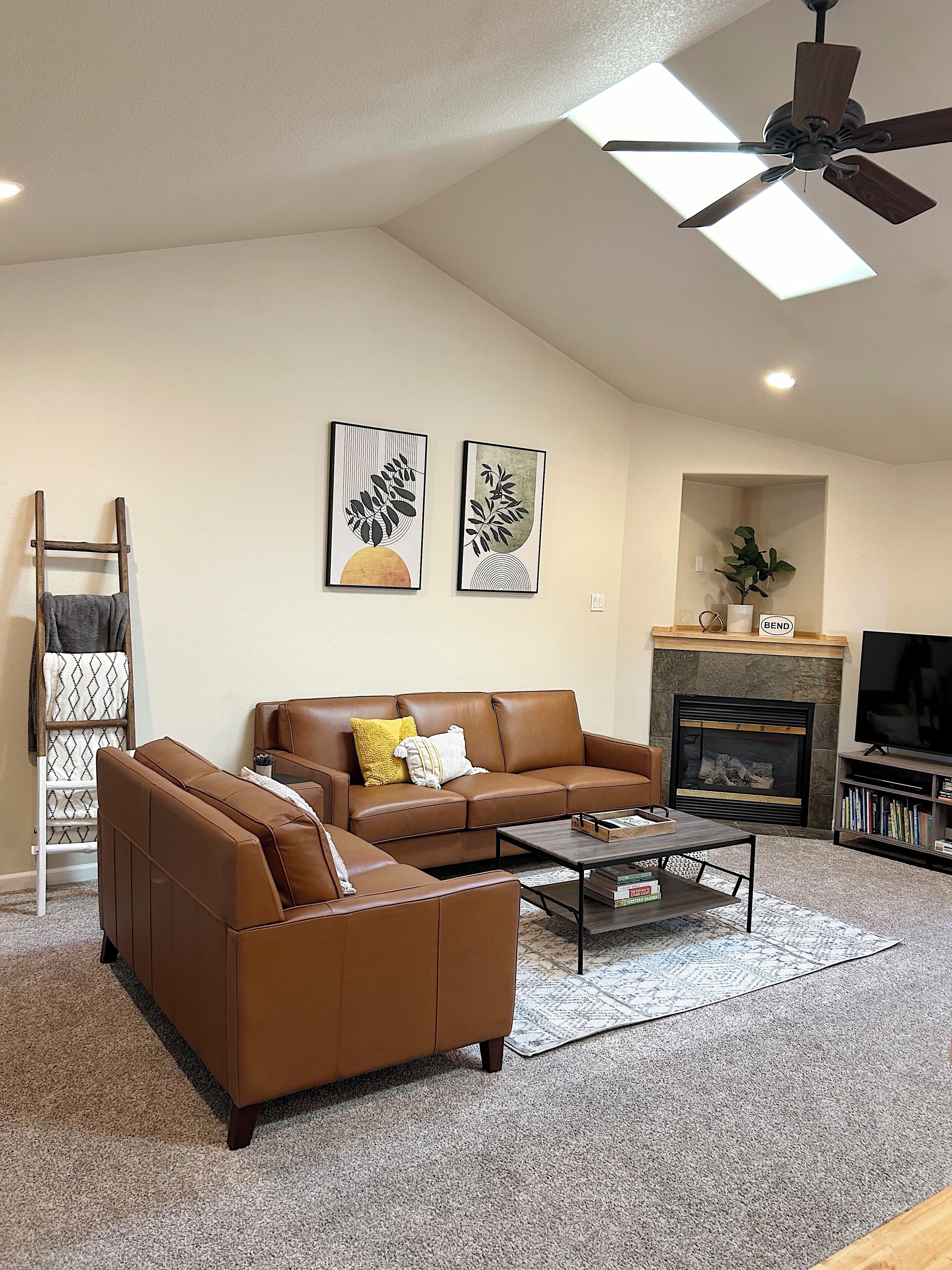 A living room with a brown leather sofa, a coffee table, a fireplace, and two framed artworks on the wall.