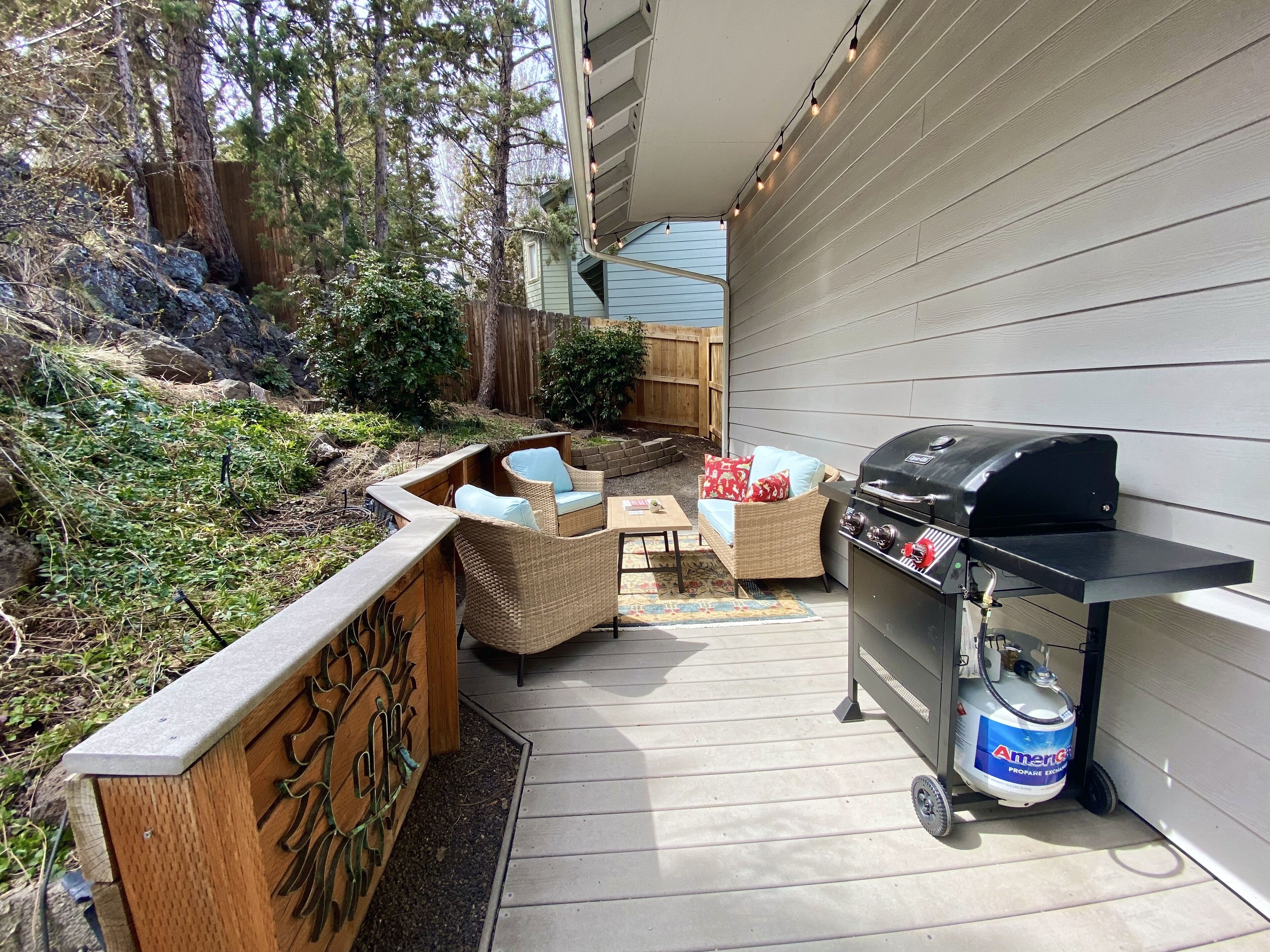 An outdoor patio with a grill, wicker furniture, and a decorative fence.