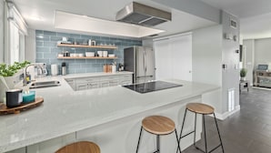 Una cocina moderna con una isla central, taburetes de bar, horno empotrado y un refrigerador de acero inoxidable.
