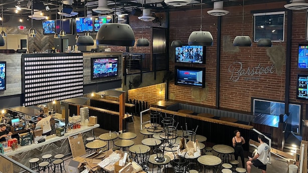 Un restaurante con varias televisiones en las paredes, una zona de bar y varias mesas redondas.