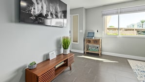 Una sala moderna con una chimenea grande en blanco y negro, una mesa consola de madera con una planta en maceta, una mesita auxiliar con un radio y un ventanal con vistas a edificios.