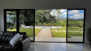 Ein modernes Wohnzimmer mit einem großen Schiebeglasfenster, das zu einem Garten mit einem Steinweg führt.