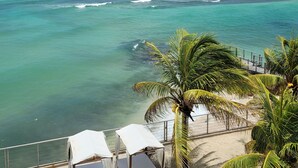 Vista de la playa con aguas turquesas cristalinas, arena dorada y algunas sillas de playa con toldos blancos.
