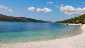 Una platja amb aigua cristal·lina, un veler i un paisatge amb muntanyes al fons.
