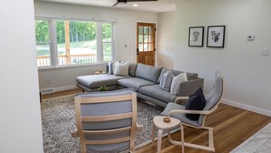 Un salon moderne avec un canapé d’angle, un fauteuil en bois et une petite table.