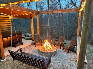Een houten gazebo met vuurkorf, zitplaatsen en een schommelbank.