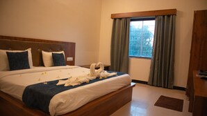 A hotel room with a large bed, a wooden headboard, a window with curtains, and a wooden desk. - PUSHKAR REGENCY RESORT (Pushkar)