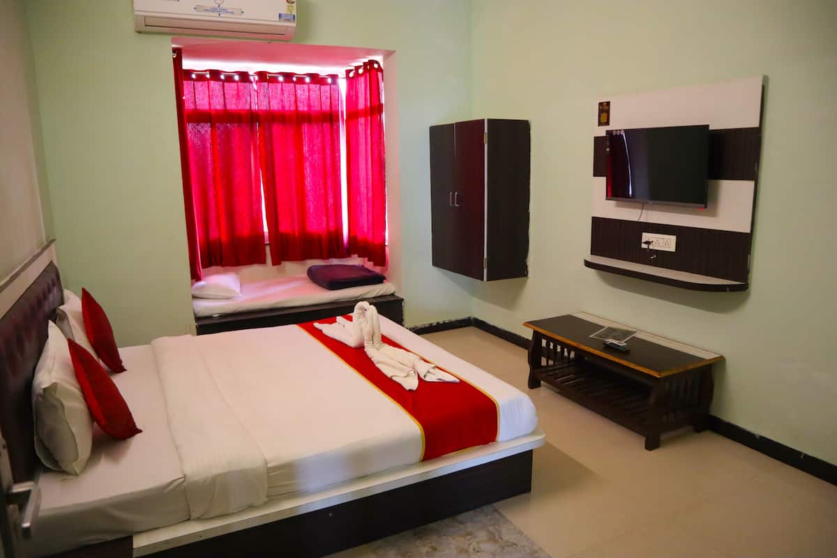 A hotel room with a bed, a TV mounted on the wall, a wardrobe, and a small table.
