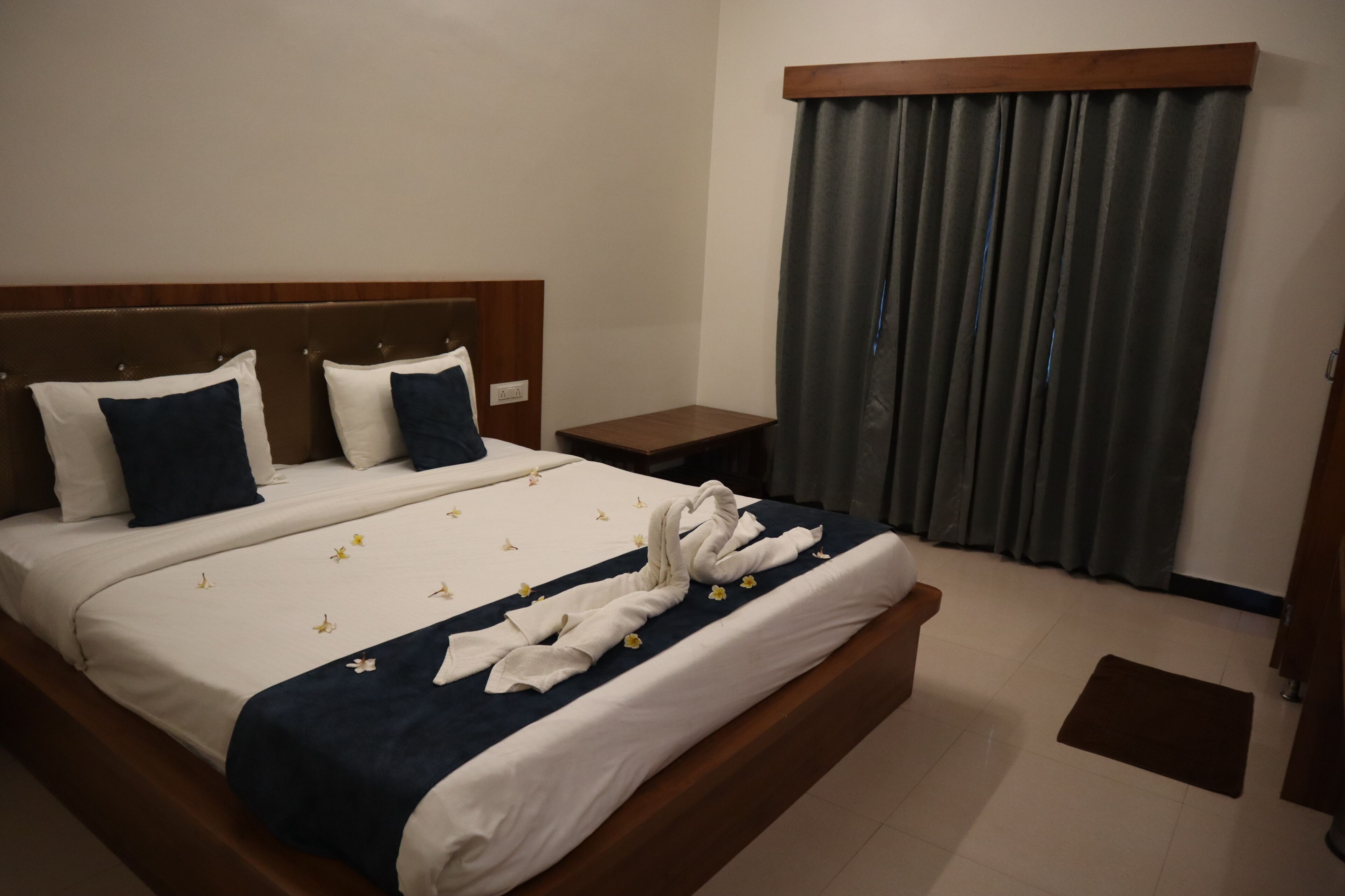 A hotel room with a bed, a nightstand, a wooden headboard, and a window with curtains.