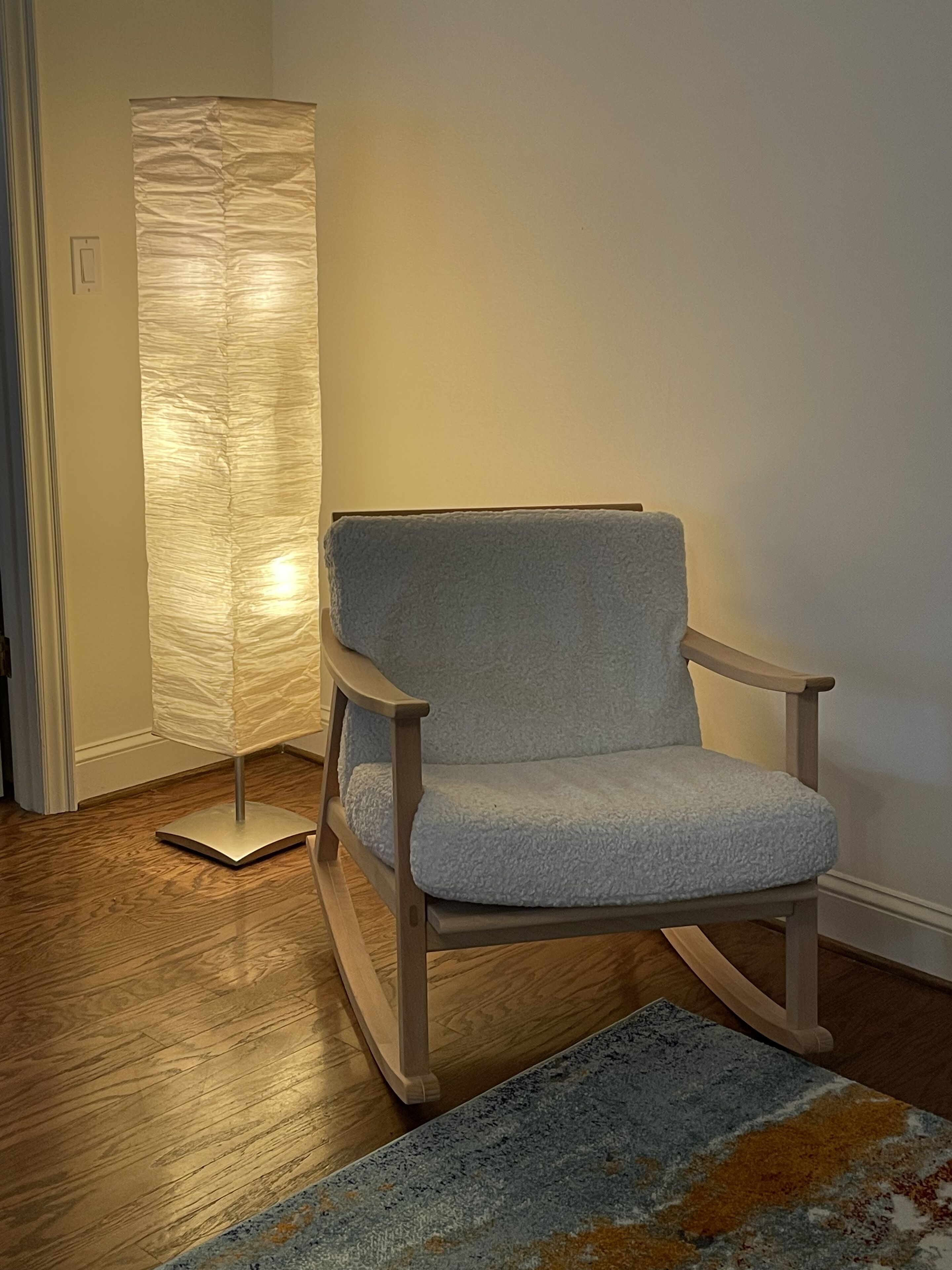Een schommelstoel met een lichtblauwe bekleding en houten frame, geplaatst op een houten vloer met een kamerbreed tapijt ervoor.