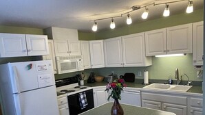 Une cuisine avec des meubles blancs, un réfrigérateur, un four à micro-ondes, une cuisinière et un évier.