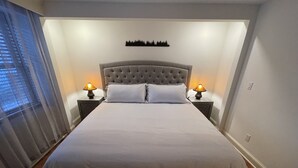 Un lit bien fait, avec une tête de lit capitonnée, deux lampes de chevet et un élément décoratif fixé au mur.