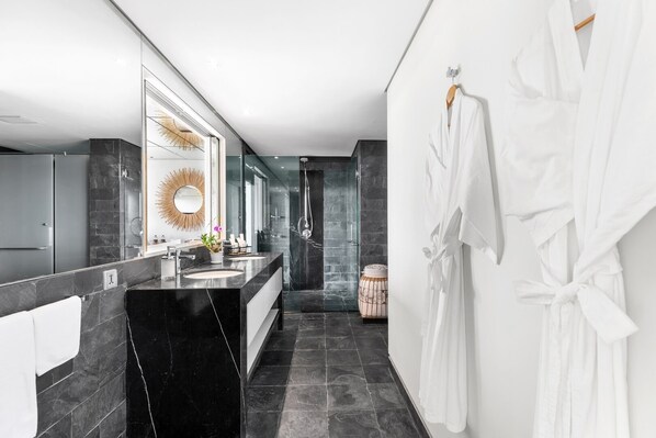 Une salle de bain moderne avec un meuble-lavabo en marbre noir, un grand miroir et un espace douche.