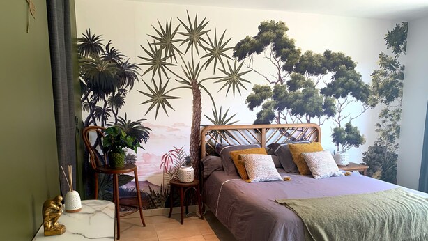Un dormitorio con cama, una silla, una mesita y un mural en la pared.