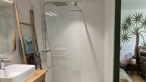 Un baño moderno con ducha acristalada, tocador de madera con lavabo blanco y un espejo.