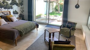 Un dormitorio con cama, una silla, una mesa y vistas al exterior por una puerta corrediza.