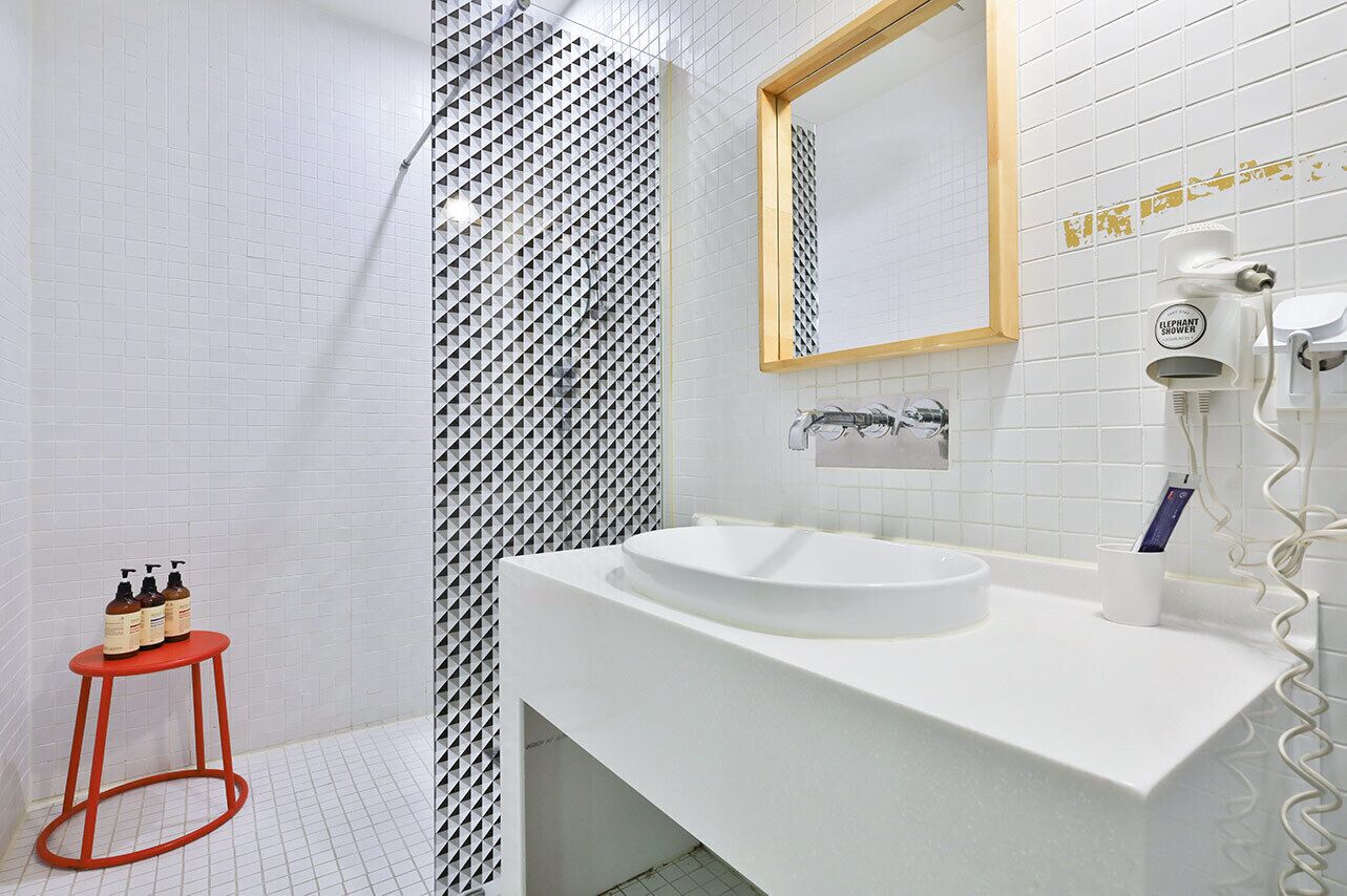 Un baño moderno con un lavamanos blanco, un espejo y una zona de ducha.