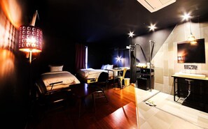 A hotel room with two beds, a desk, a chair, a desk lamp, a TV, and a bathroom with a sink and mirror. - Elephant Shower Hotel (Jinju)