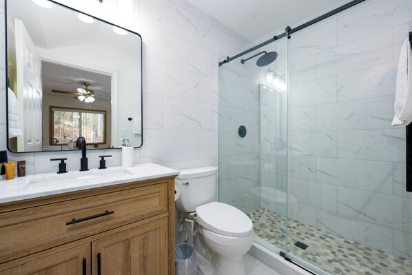 Un baño moderno con lavamanos de mármol blanco, tocador de madera, ducha con cerramiento de vidrio y un inodoro.