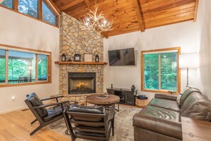 Una sala de estar acogedora con chimenea de piedra, mobiliario de cuero y ventanas amplias con vistas al exterior.