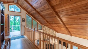 Un interior espacioso con una escalera de madera, una chimenea de piedra y grandes ventanales con vistas al exterior.