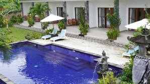 A swimming pool with lounge chairs and umbrellas, surrounded by greenery and a stone statue. - Artaloka Hotel & Restaurant (Penida Island)