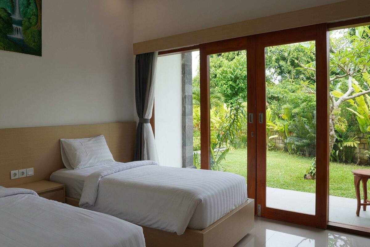 Een hotelkamer met twee bedden, een grote schuifdeur naar een tuin en een schilderij aan de muur.