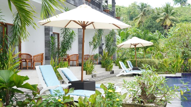 A poolside area with lounge chairs, umbrellas, and lush greenery. - Artaloka Hotel & Restaurant (Penida Island)