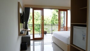 A hotel room with a bed, a TV, a desk, and a balcony with a view of greenery. - Artaloka Hotel & Restaurant (Penida Island)