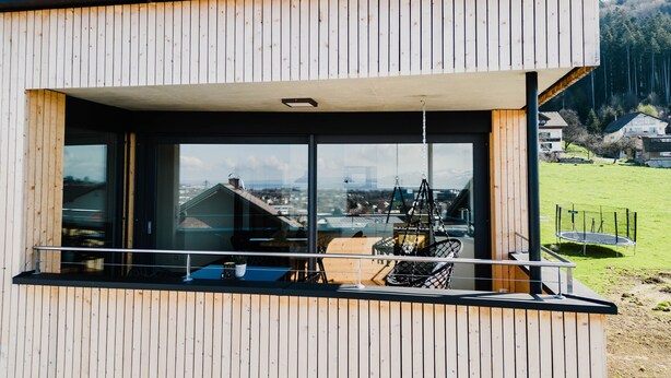 Un bâtiment moderne en bois, doté de grandes fenêtres qui offrent une vue sur un paysage verdoyant et sur des bâtiments situés au loin.