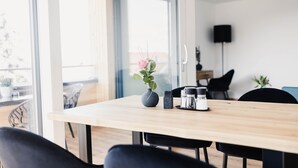 Un espace repas moderne avec une table en bois, des chaises noires, un vase avec une fleur et une machine à café.