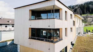 A modern two-story building with a wooden facade, large windows, and a balcony. - Elegant 2-room vacation apartment (1st floor) with 49sqm & covered balcony, close to the lake (Gemeinde Hörbranz)