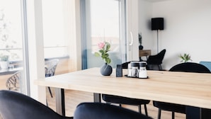 A modern dining area with a wooden table, black chairs, a vase with a flower, and a coffee maker. - Elegant 2-room vacation apartment (1st floor) with 49sqm & covered balcony, close to the lake (Gemeinde Hörbranz)