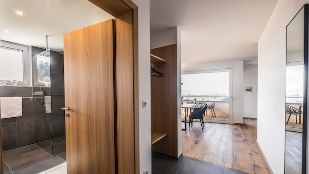 A modern interior with a wooden door, a shower area, and a dining space with a view. - Elegant 2-room vacation apartment (1st floor) with 49sqm & covered balcony, close to the lake (Gemeinde Hörbranz)