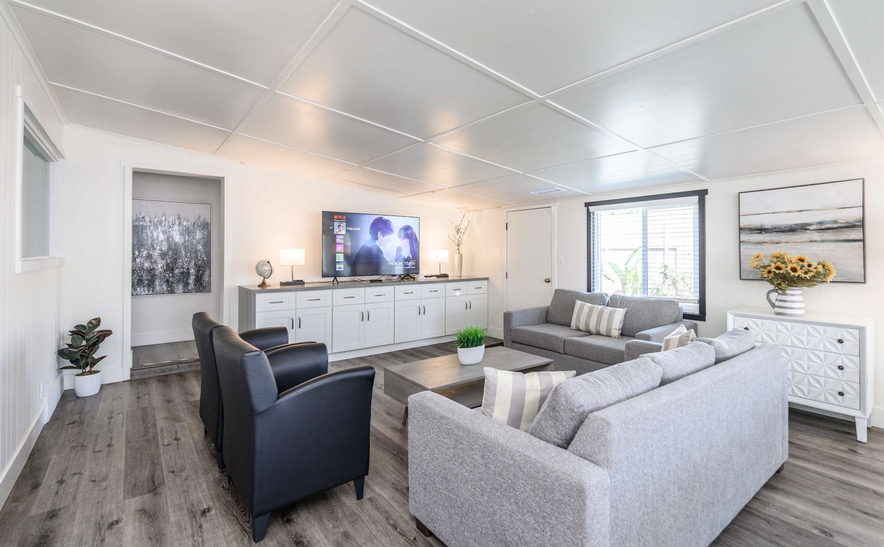 Un salon moderne avec un téléviseur à écran plat, des canapés gris, une table basse et un meuble blanc.