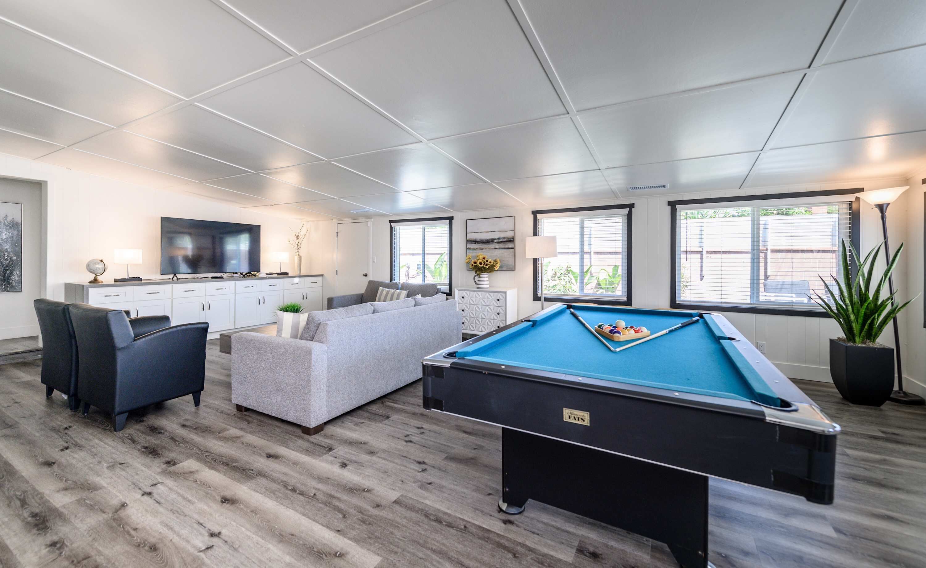 A modern living room with a pool table, a sofa, a television, and a kitchen area.