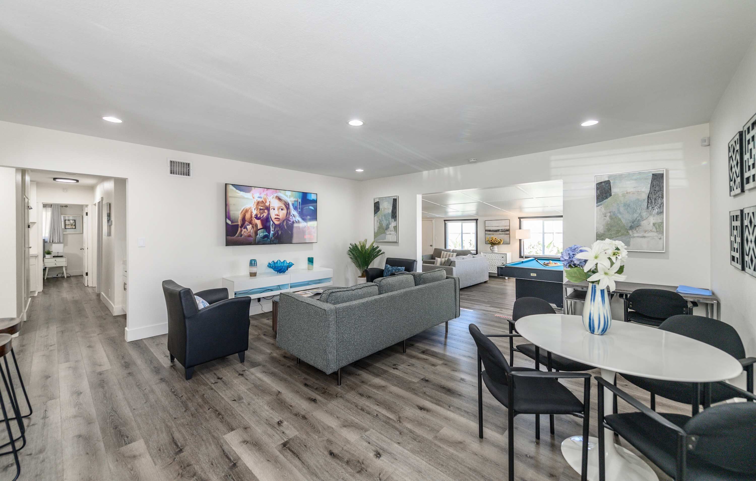 A spacious living area with a grey sofa, a dining table with chairs, and a pool table.
