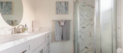 A bathroom with a marble sink, a glass shower enclosure, and a patterned floor.