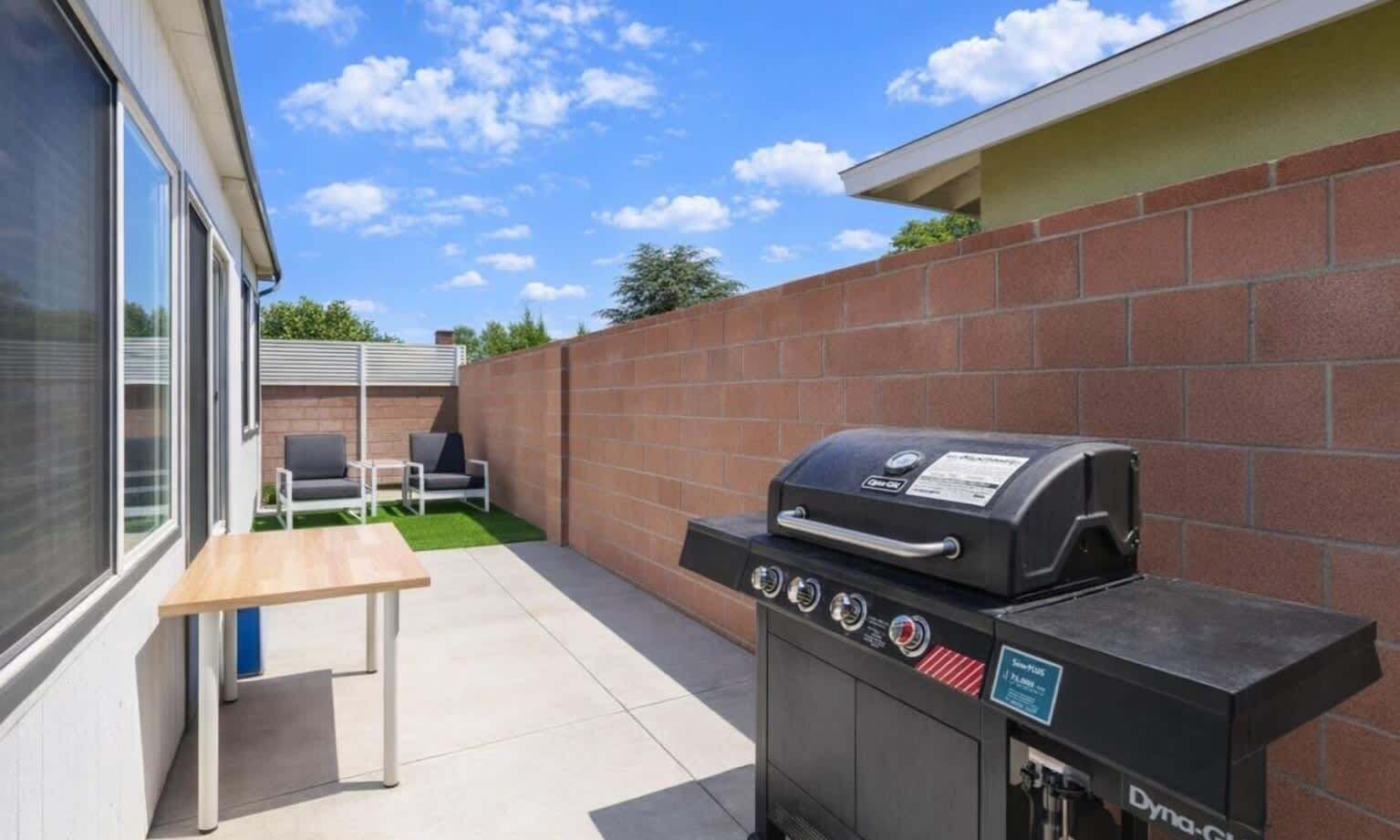 Une terrasse avec un barbecue, une table et deux chaises.